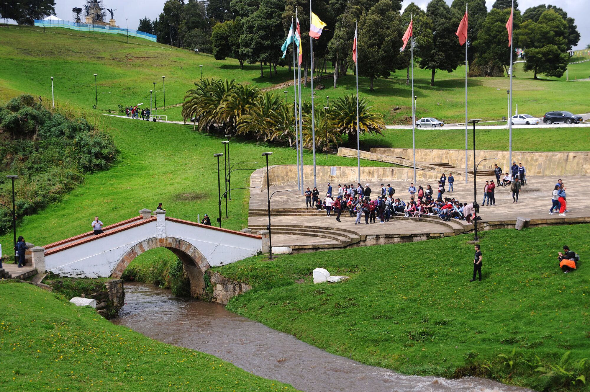 A park with a bridge, a group of people, and flags.