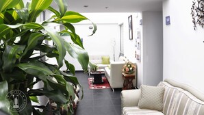 A modern hotel living room with a large green plant, a white sofa, and a small table with a vase of flowers.