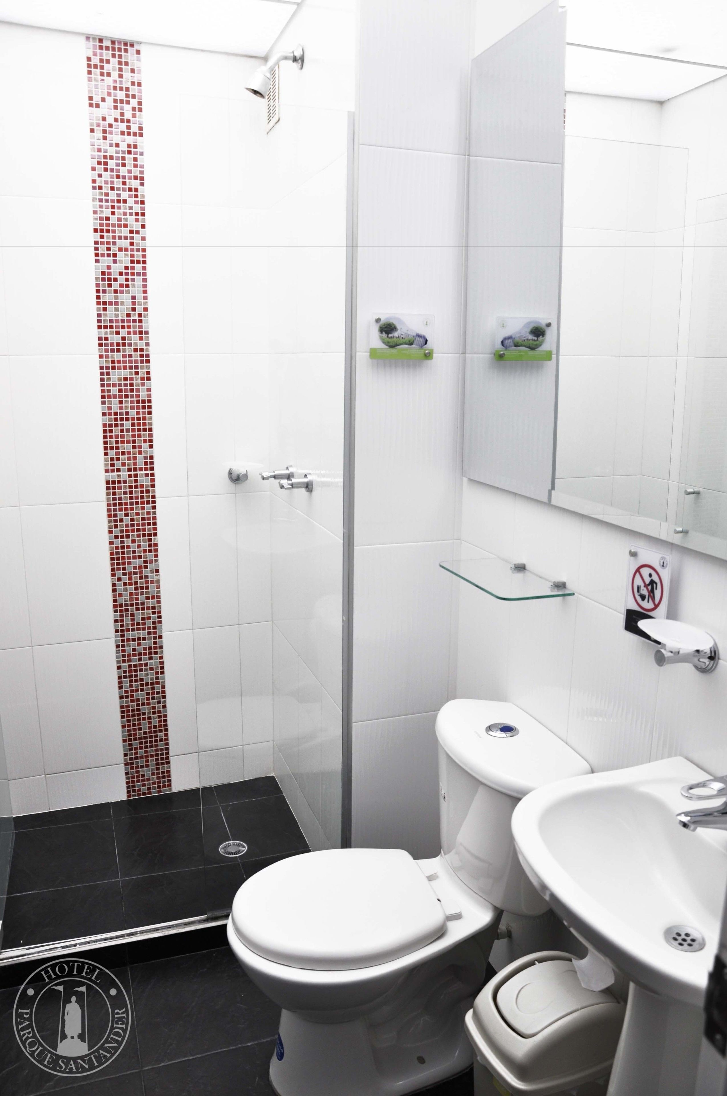 A modern bathroom with a white toilet, a sink, and a shower. There is a glass shelf above the sink and a glass door leading to the shower.