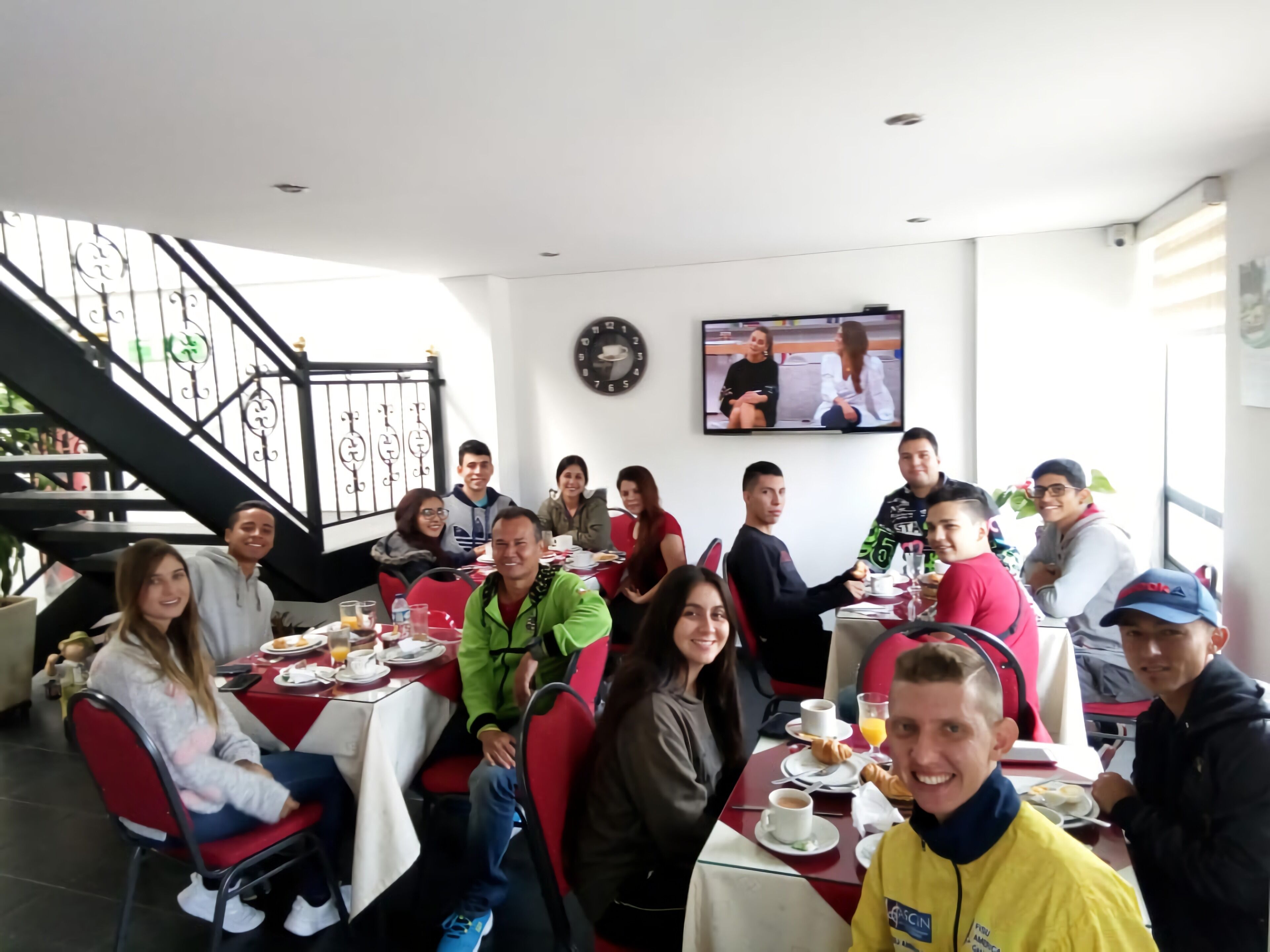 A group of people dining in a restaurant with a staircase and a TV on the wall.