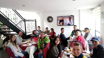 A group of people dining in a restaurant with a staircase and a TV on the wall.