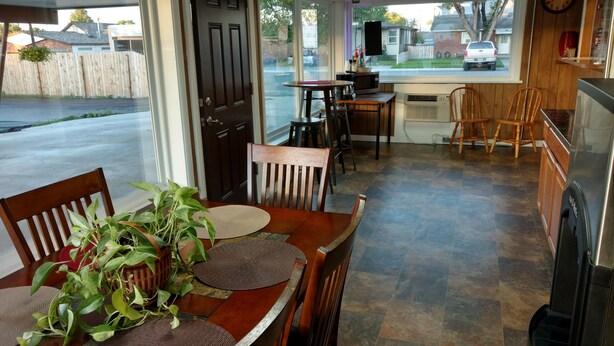 A dining area with a table set for two, a potted plant, and a view of the street through large windows. - Cattlemen Motel (Lovell)