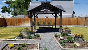 A wooden pergola with a bench in a backyard garden with flower beds and a wooden fence. - Cattlemen Motel (Lovell)