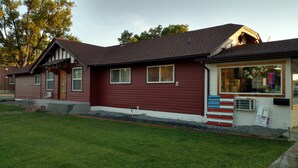 A two-story building with a red exterior, a small front porch, and a visible garage. - Cattlemen Motel (Lovell)