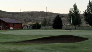A golf course with bunkers, a wooden cabin, and a mountainous backdrop. - Cattlemen Motel (Lovell)