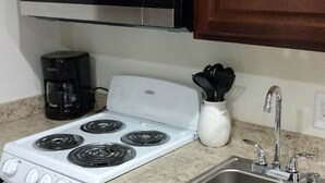 A kitchen with a white stove, a black microwave, a coffee maker, a sink, and wooden cabinets. - Cattlemen Motel (Lovell)