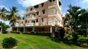 A multi-story hotel with balconies, surrounded by palm trees and a well-maintained lawn. - Hotel Coco Plaza (Las Terrenas)