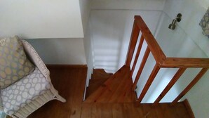 A wooden staircase leading to a landing with a white wall and a patterned cushion on a chair. - Hotel Coco Plaza (Las Terrenas)