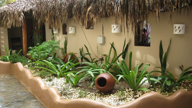 A courtyard with a curved wall, potted plants, and a thatched roof structure. - Hotel Coco Plaza (Las Terrenas)