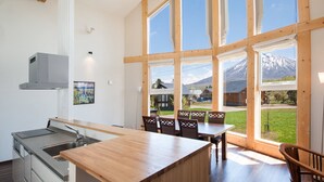 A modern kitchen with a large island, wooden chairs, and a view of a mountain through large windows. - The Orchards Niseko (Kutchan)