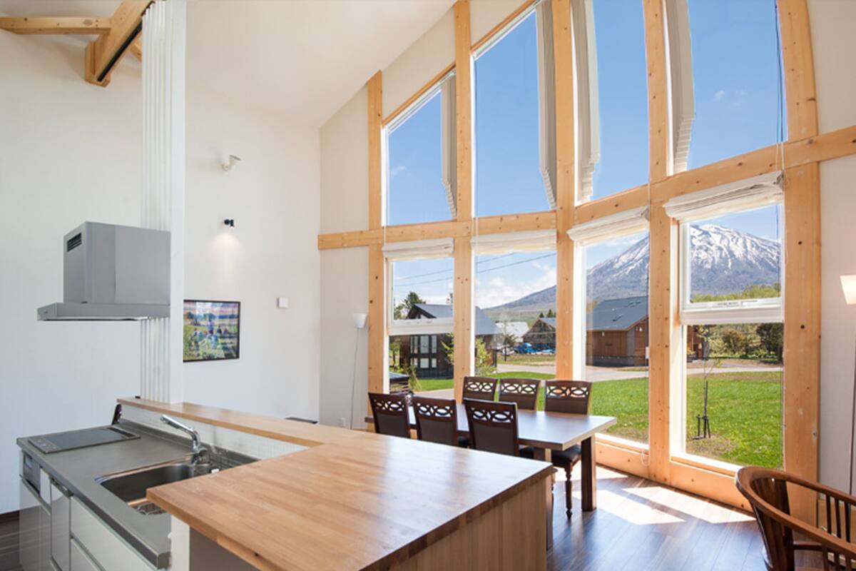 A modern kitchen with a large island, wooden chairs, and a view of a mountain through large windows.