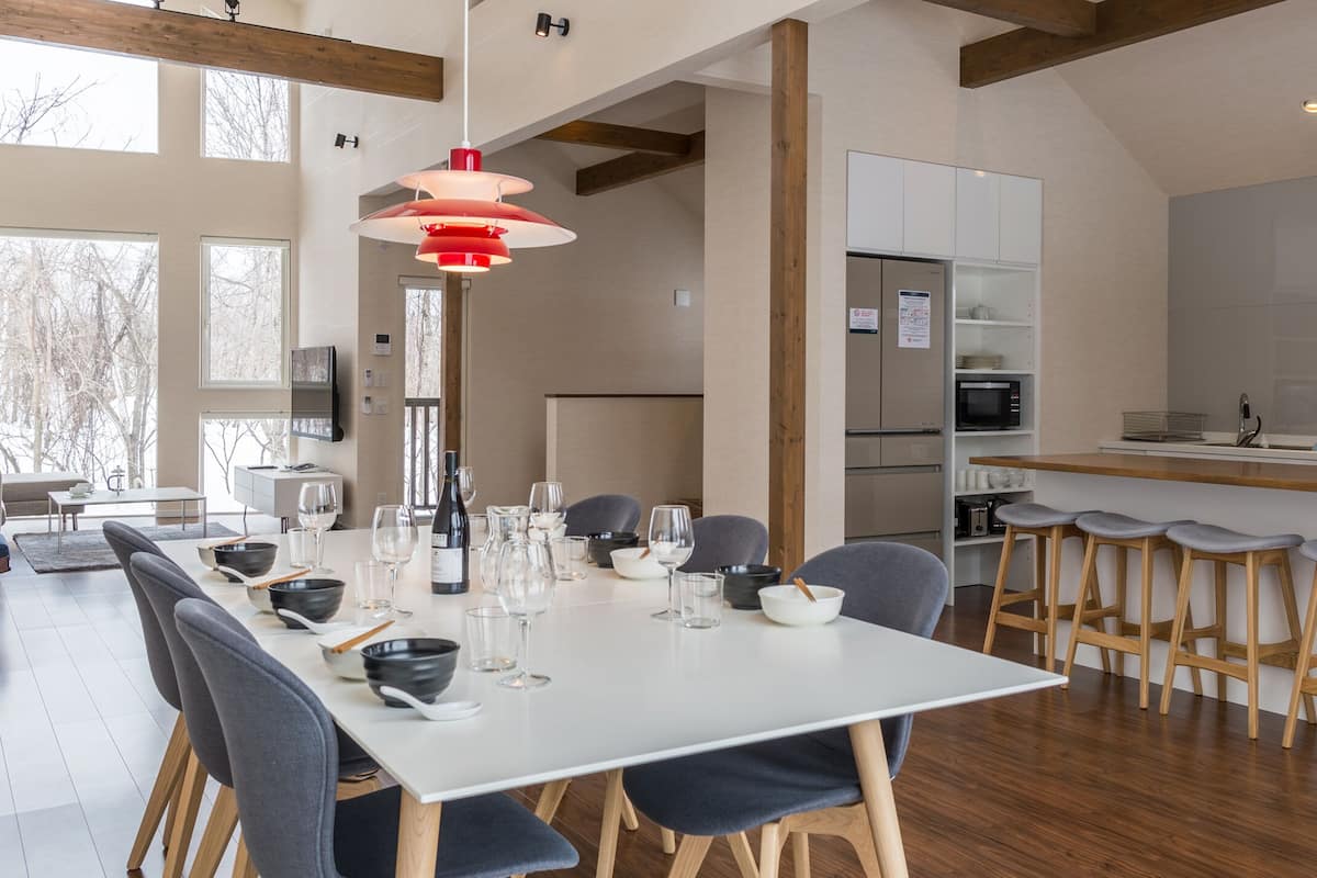 A modern kitchen with a central island, bar stools, and a dining area with a white table and chairs.
