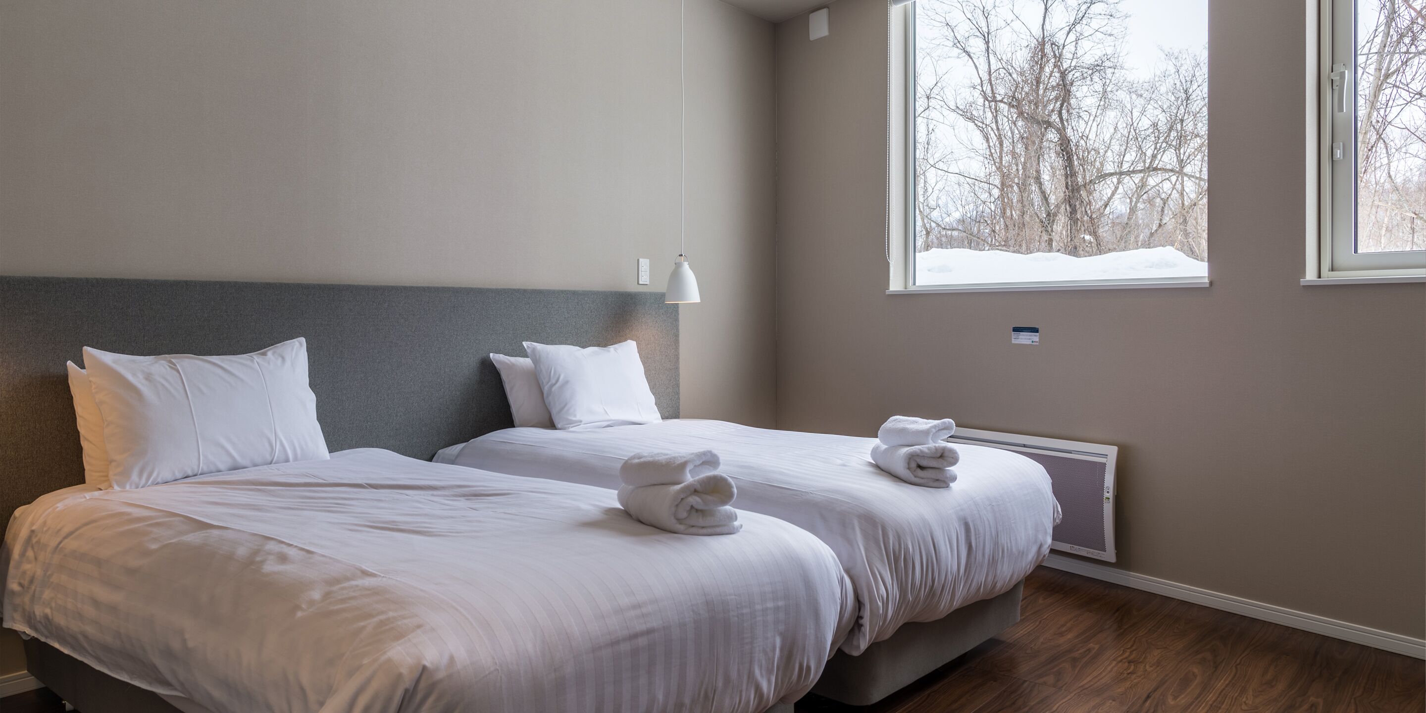 A hotel room with two beds, a large window with a view of trees, and a wall-mounted air conditioner.