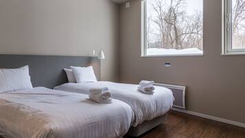 A hotel room with two beds, a large window with a view of trees, and a wall-mounted air conditioner.