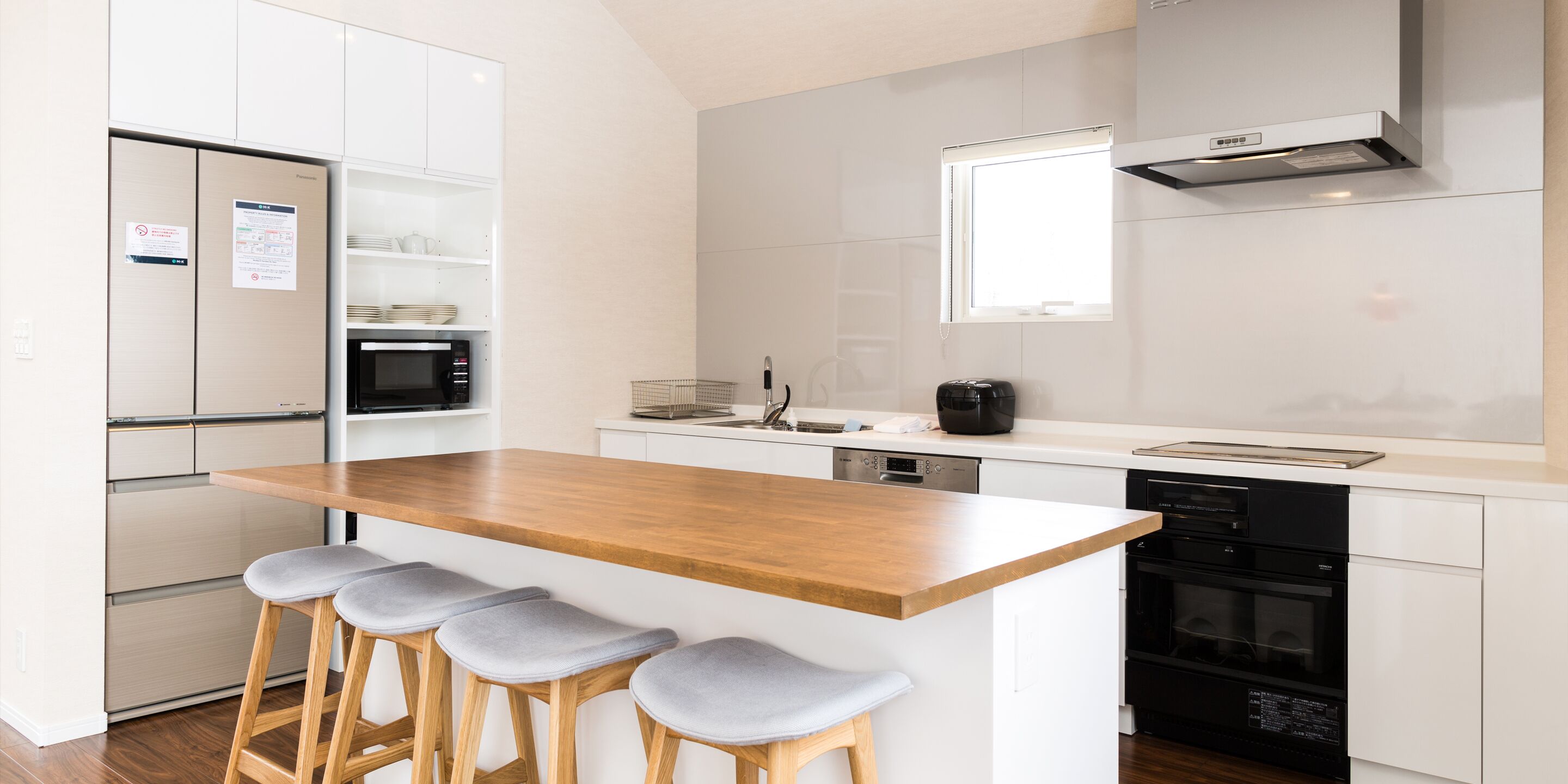 A modern kitchen with white cabinetry, a wooden island with bar stools, a microwave, a coffee maker, and a dishwasher.