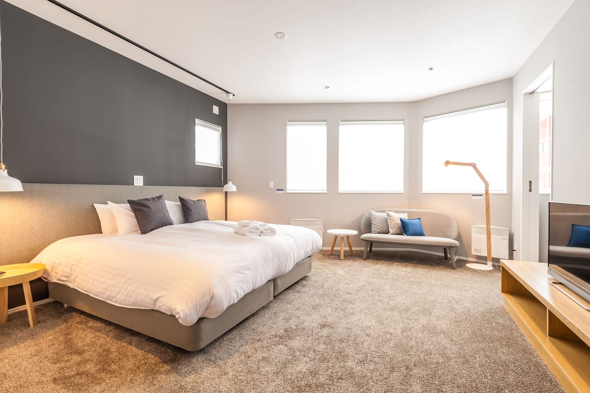 A modern bedroom with a large bed, a sofa, a TV, and a desk.