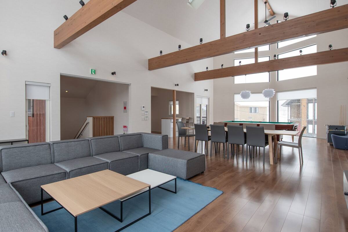 A modern lounge with a sectional sofa, a pool table, and a dining area with chairs and tables.