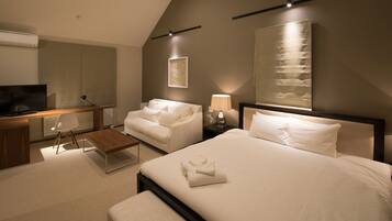 A modern hotel room with a large bed, a sofa, a desk with a TV, and a flat-screen TV.