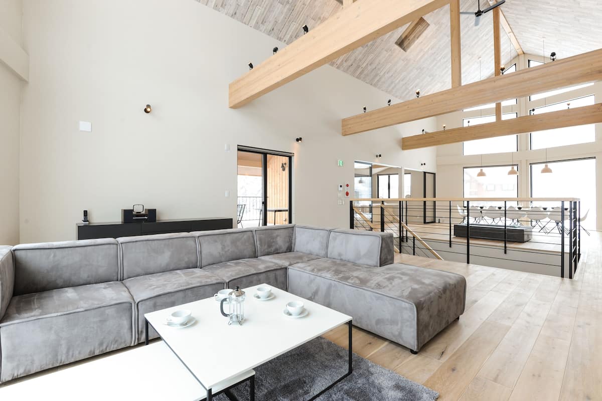 A spacious living area with a large gray sectional sofa, a white coffee table, and a staircase leading to an upper level.