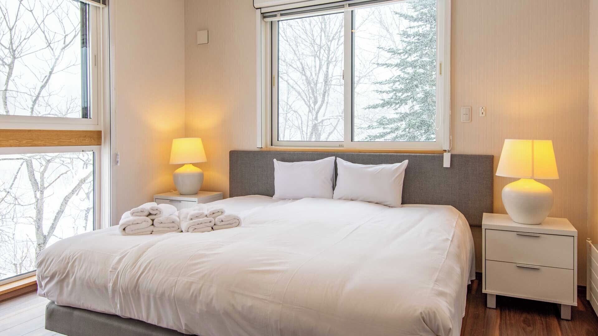 A neatly made bed with white linens, two bedside lamps, and a stack of folded towels on the nightstand.