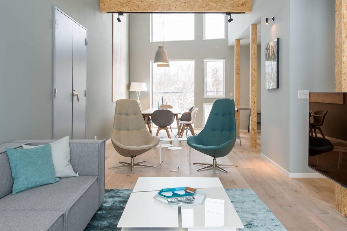A modern living room with a grey sofa, teal and beige chairs, a white coffee table, and a TV on the right.