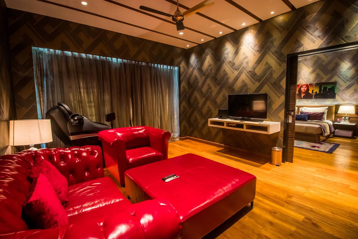 Una habitación de hotel moderna con un sofá de cuero rojo, un televisor y una cama con un mural de paisaje urbano.