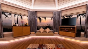 A modern living room with a large flat-screen TV, wooden furniture, and a view of the beach through a large window. - Planet Hollywood Goa Beach Resort (Utorda)