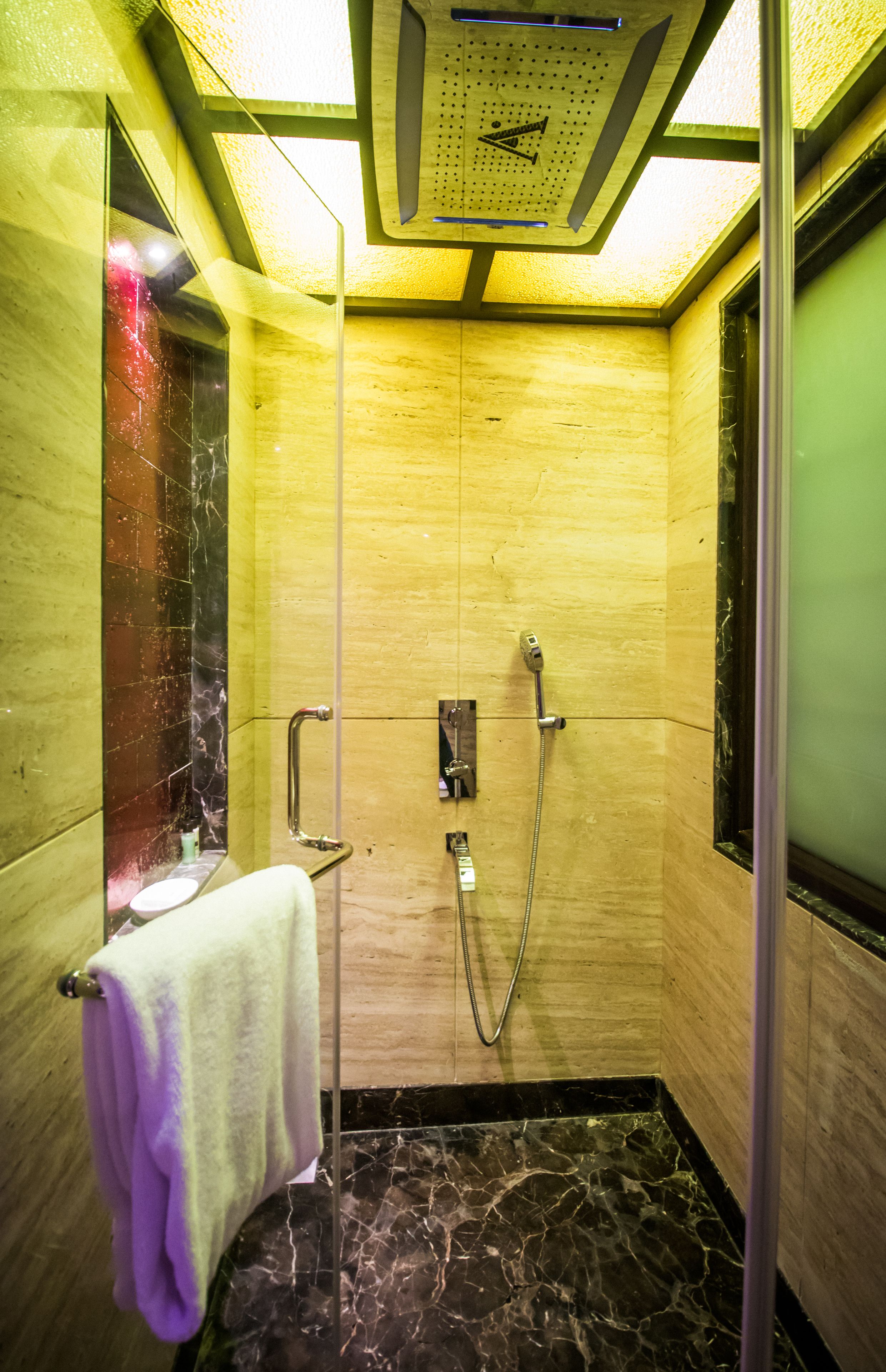 Un piccolo bagno rivestito di piastrelle con porta in vetro, un asciugamano appeso al muro e un soffione a parete.