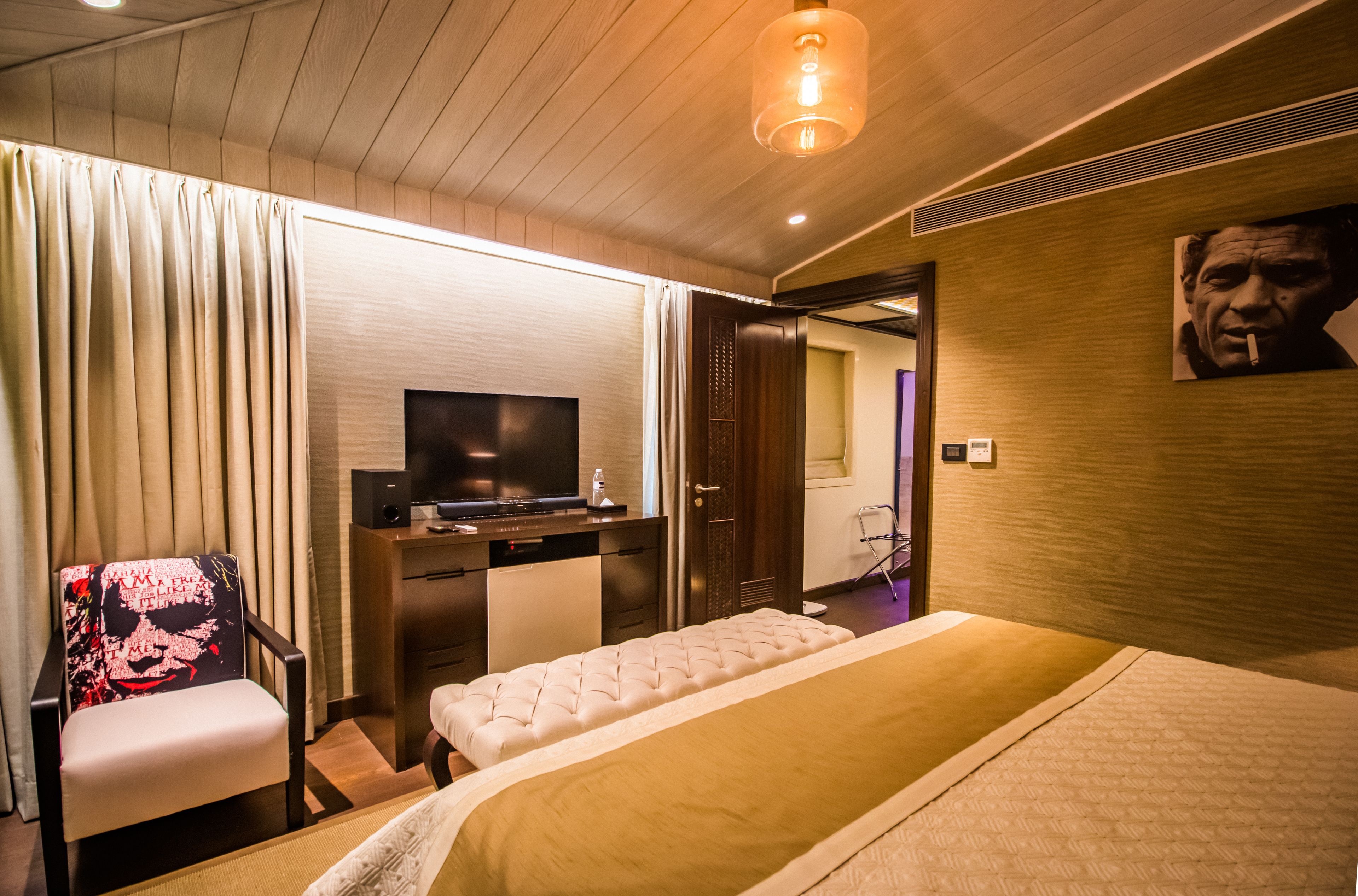 A hotel room with a bed, a desk, a chair, a television, and a painting on the wall.