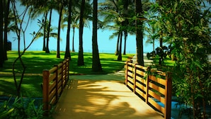A wooden pathway leading to a beach, surrounded by palm trees and greenery. - Planet Hollywood Goa Beach Resort (Utorda)