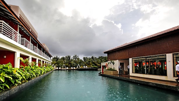 A pool area with a long corridor, a red building, and a glass-walled structure. - Planet Hollywood Goa Beach Resort (Utorda)
