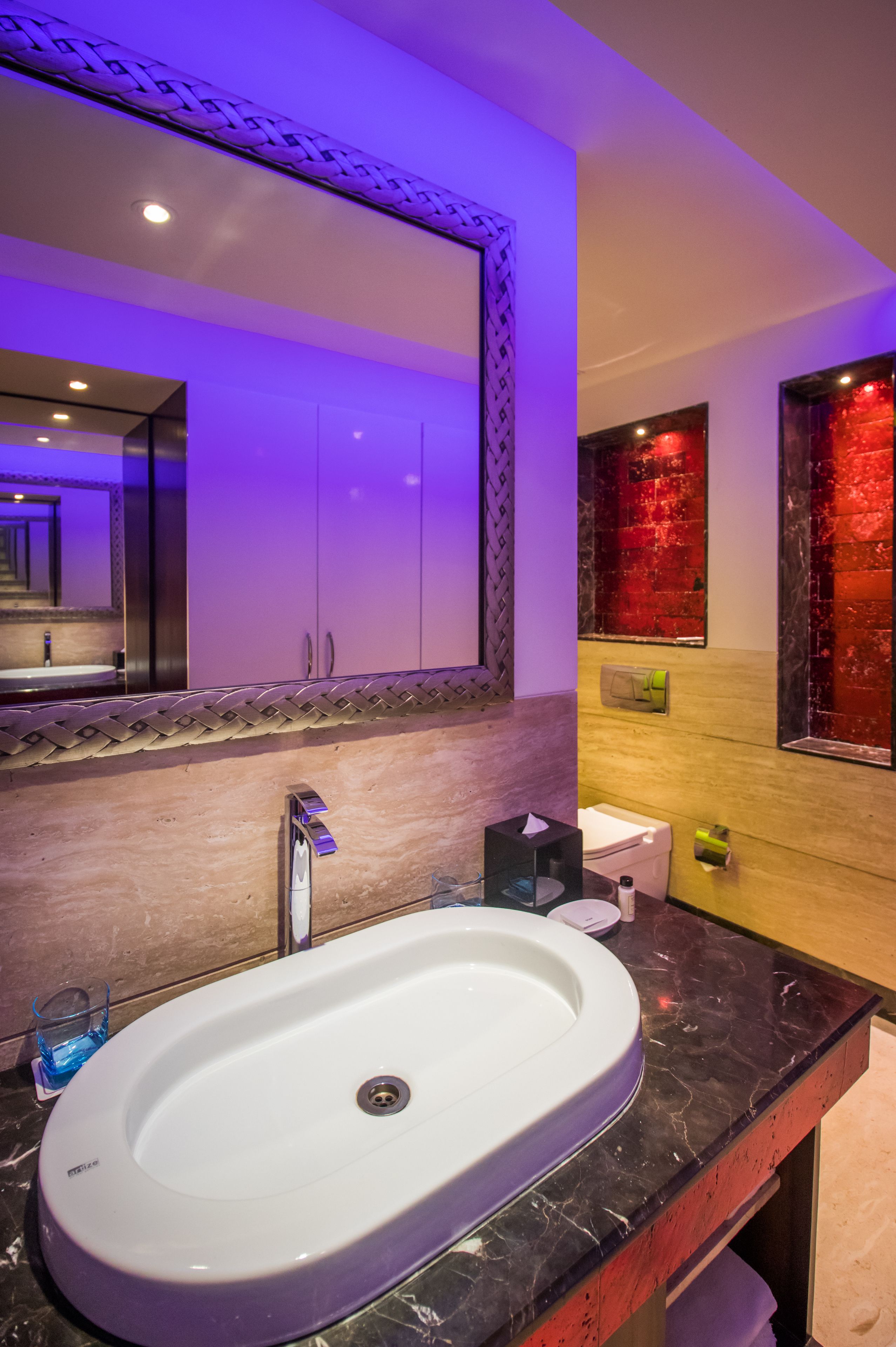 Un bagno moderno con un lavandino bianco, uno specchio grande e una parete decorata di rosso.
