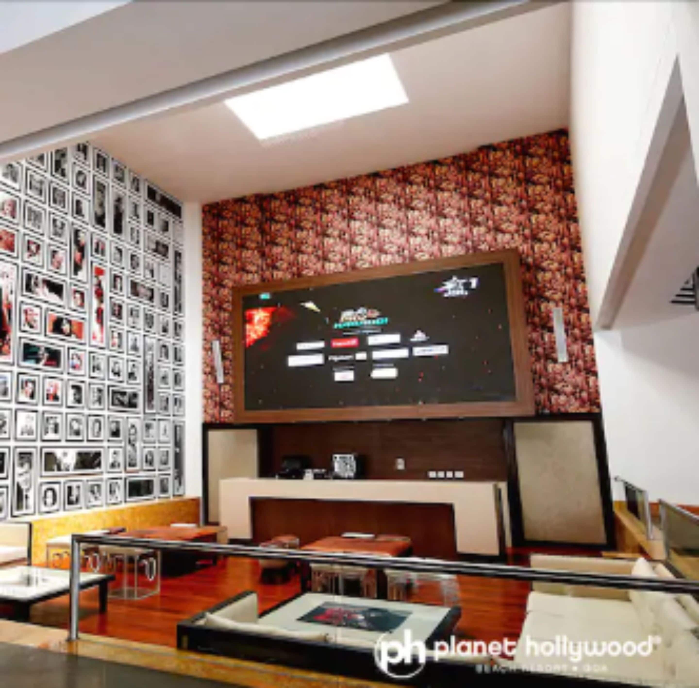 Una habitación con un televisor de pantalla plana grande montado en una pared con papel tapiz floral, suelo de madera y una pared llena de fotografías enmarcadas.