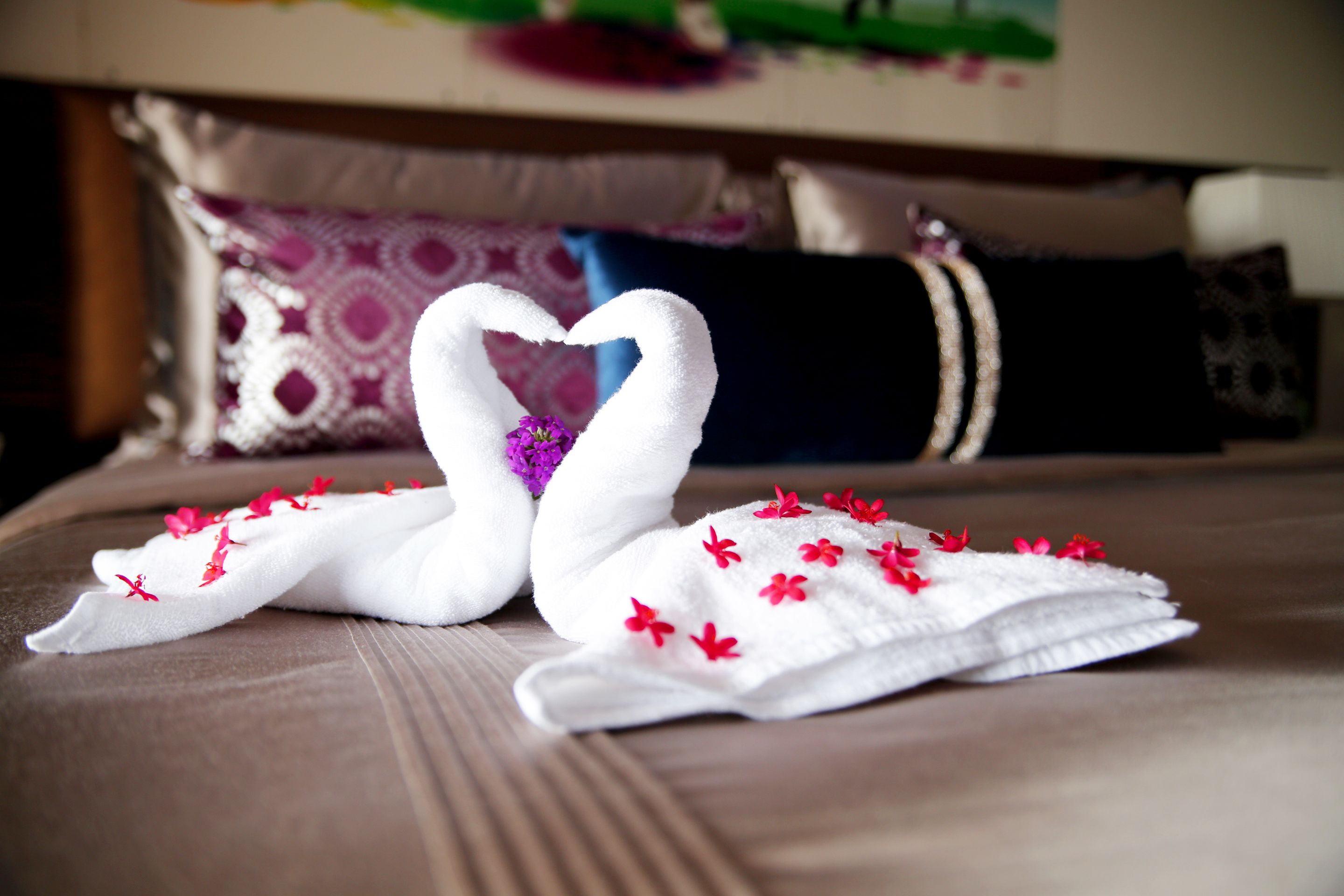 Un lit agrémenté d’une décoration en forme de cygne réalisée avec des serviettes et de fleurs rouges.