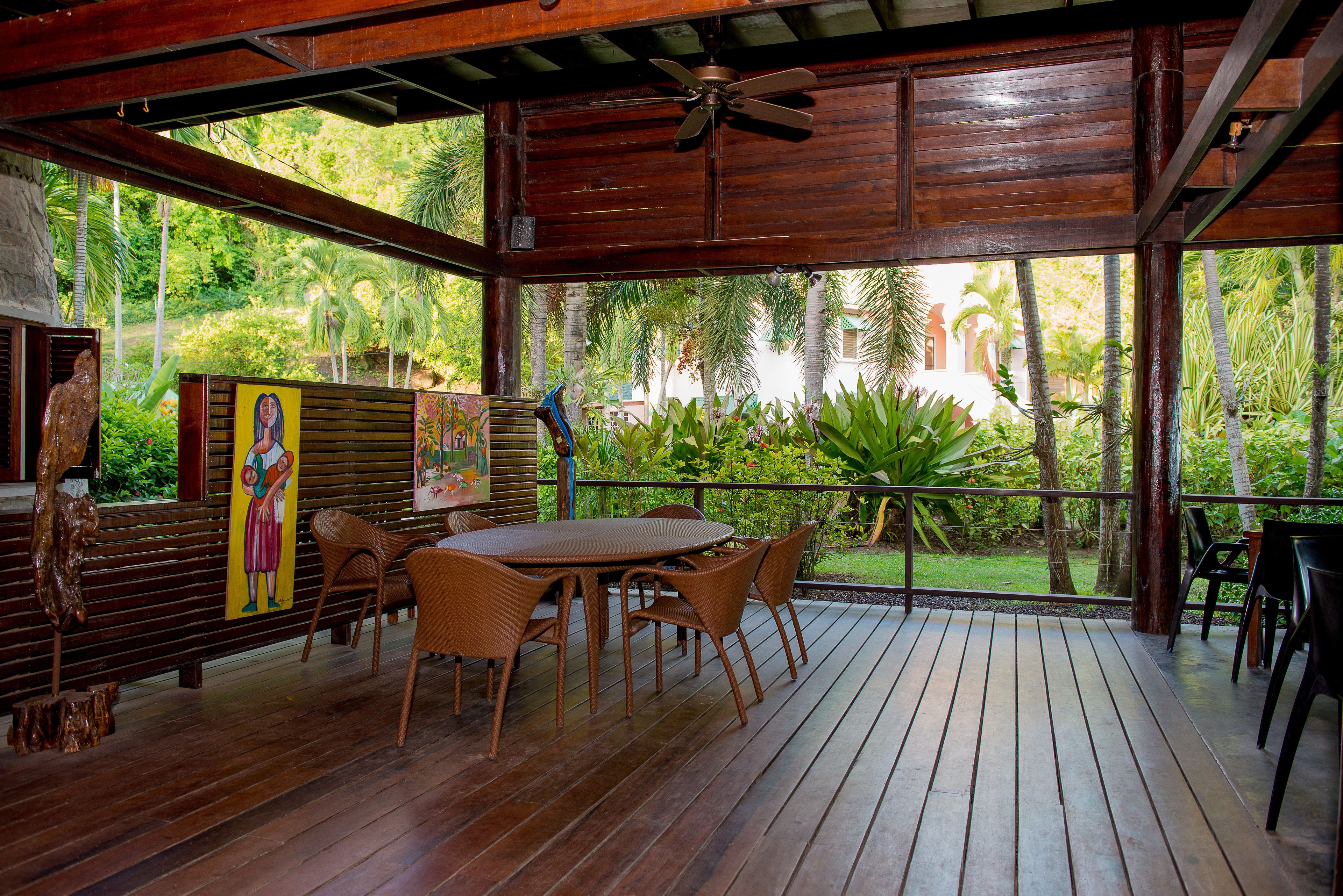 A wooden deck with a table and chairs, surrounded by lush greenery and a view of palm trees.