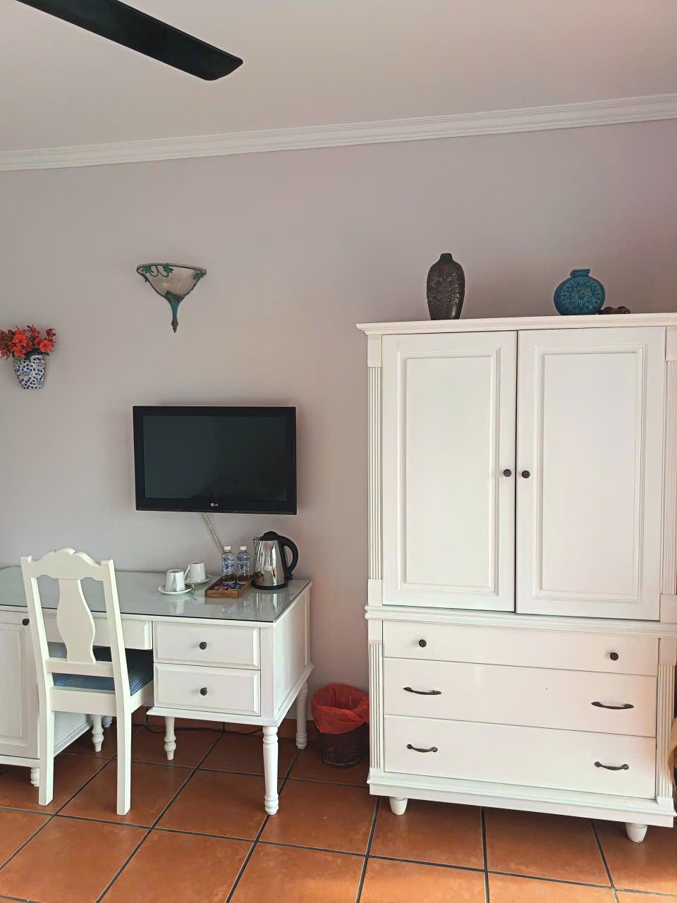A room with a white desk, a television, a white cabinet, and a tiled floor.