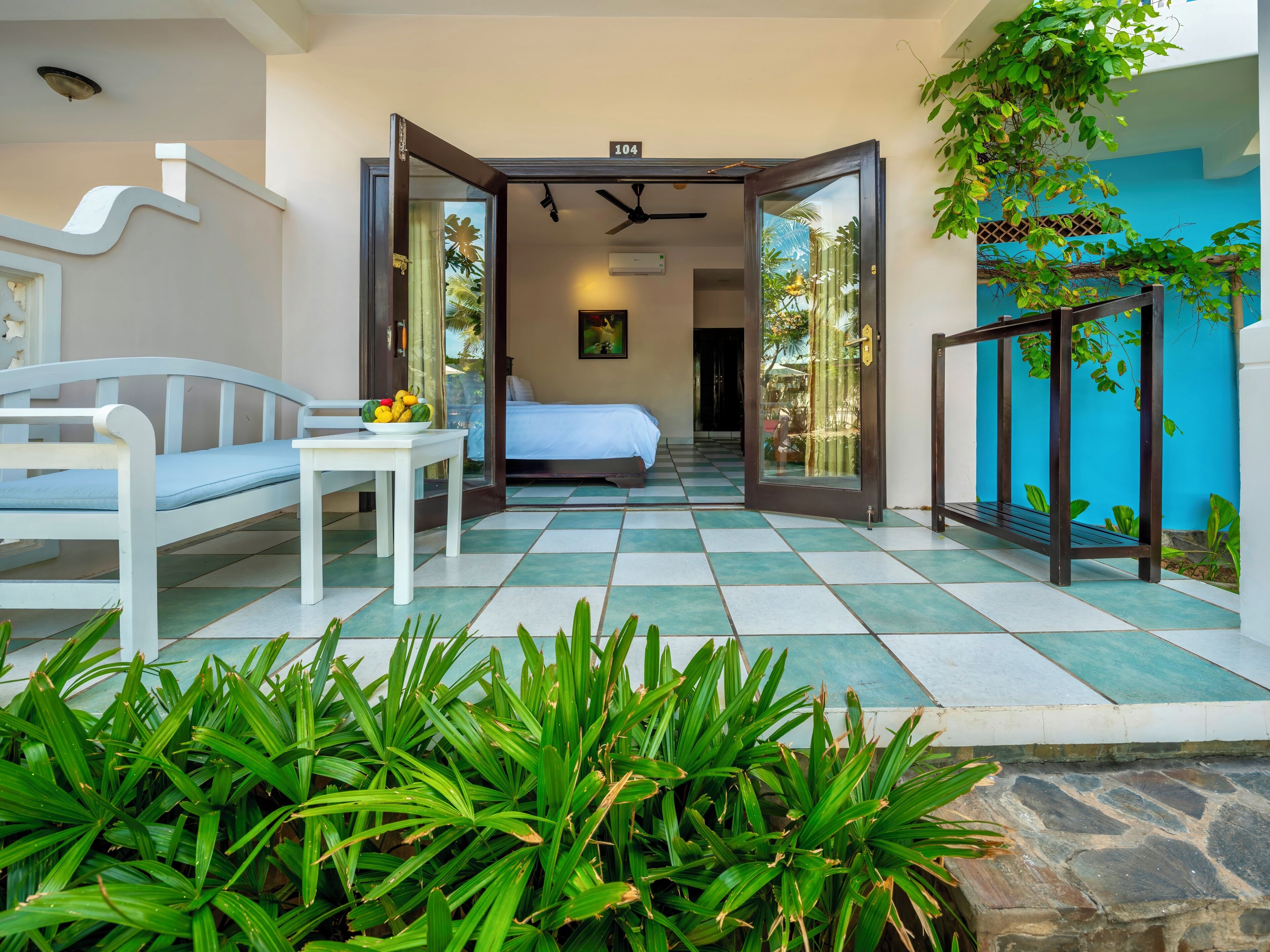 Une chambre d’hôtel avec un lit, une petite table sur laquelle se trouvent des fruits, et une vue sur le jardin.