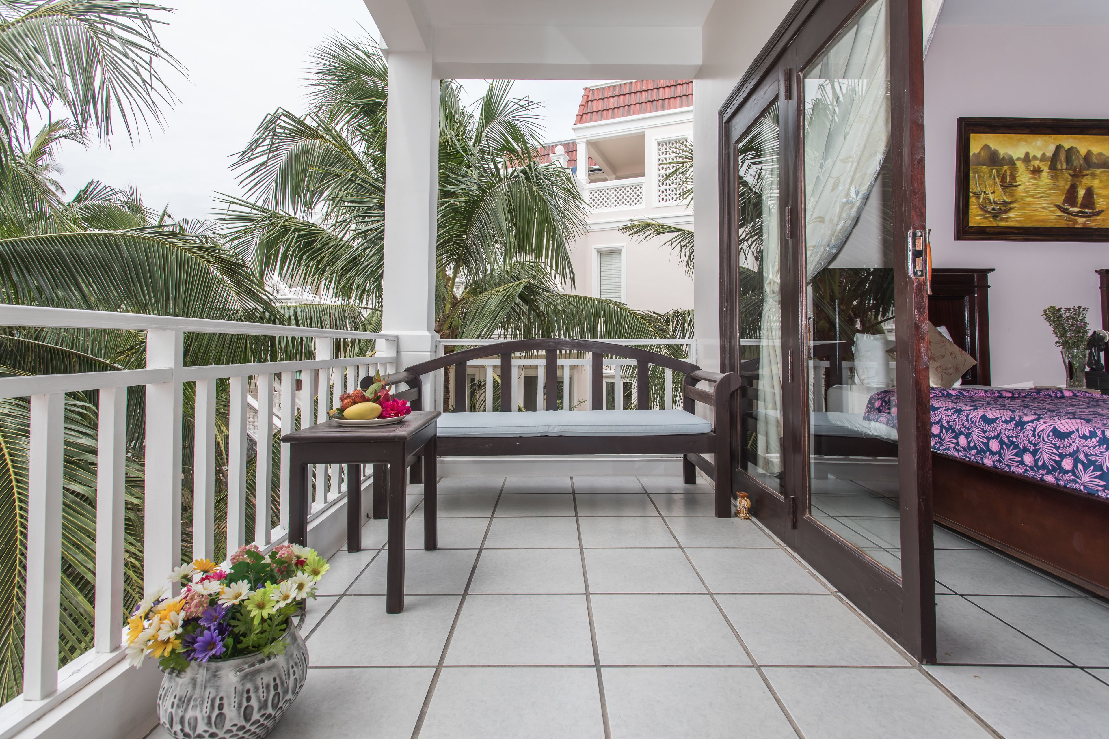 Ein Balkon mit einer Holzbank, einem kleinen Tisch mit Obst und einer Blumenvase.
