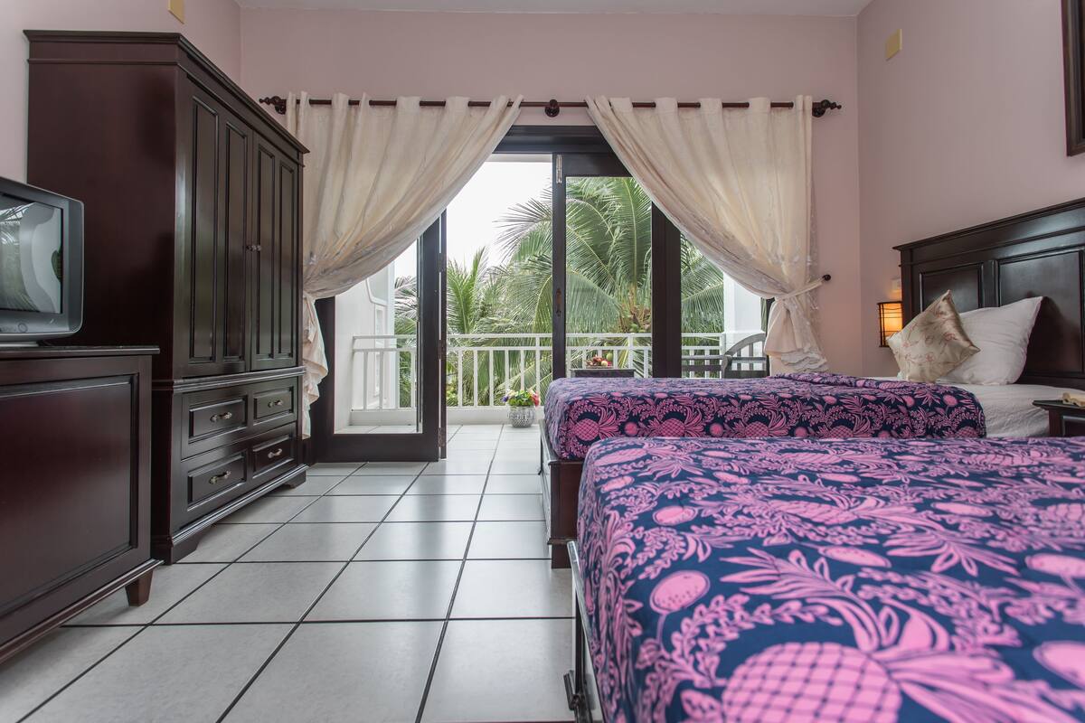Een hotelkamer met balkon, televisie, bed met beddengoed met dessin en donker houten garderobe.