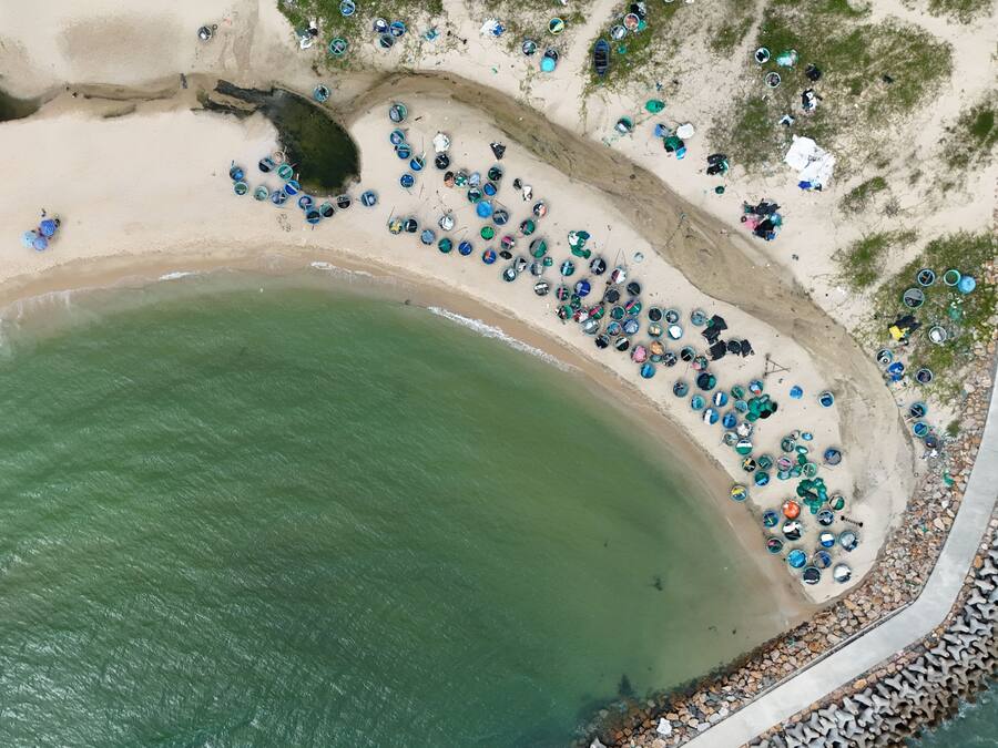 Vue aérienne d’une plage où l’on peut voir de nombreux conteneurs ronds dispersés le long du rivage.