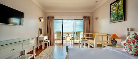 A hotel room with a bed, a desk, a chair, a TV, and a balcony with a view of the sea.