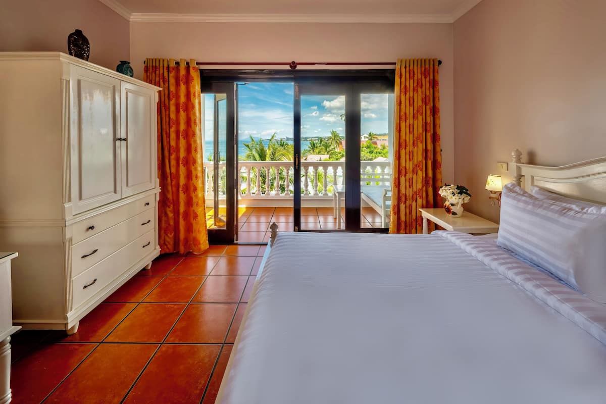 Hotelkamer met een groot bed, een kledingkast, een nachtkastje met lamp en een balkon met uitzicht op zee.