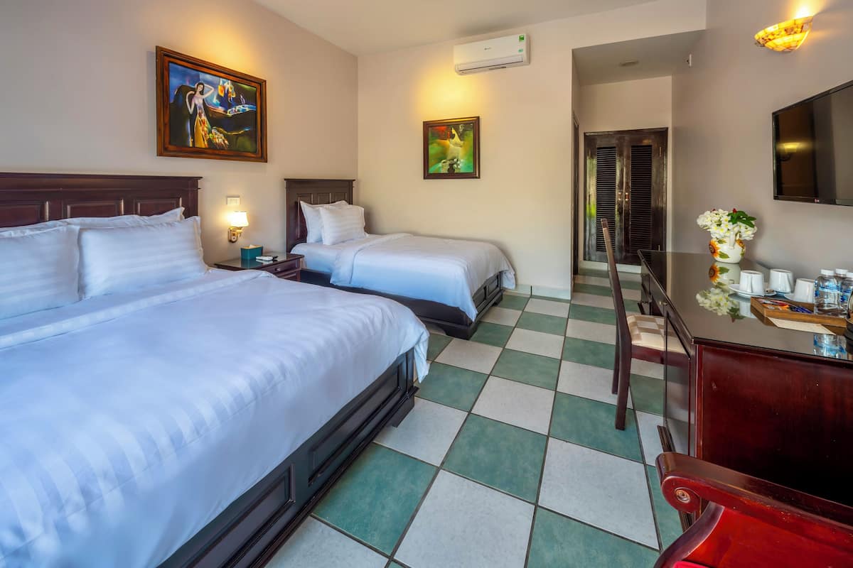 Een hotelkamer met twee bedden, een bureau, een stoel, een televisie en kunstwerken aan de wanden.