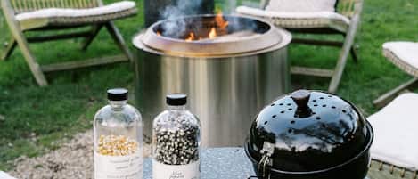 Ett runt utomhusbord med en eldstad, två glasburkar med spannmål och en svart grill.