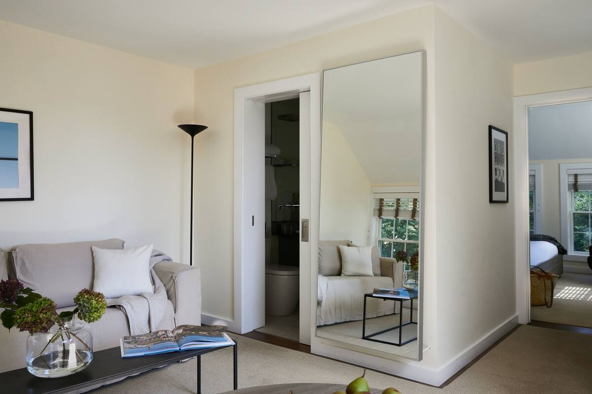 A modern living room with a sofa, coffee table, and a large mirror reflecting the room.