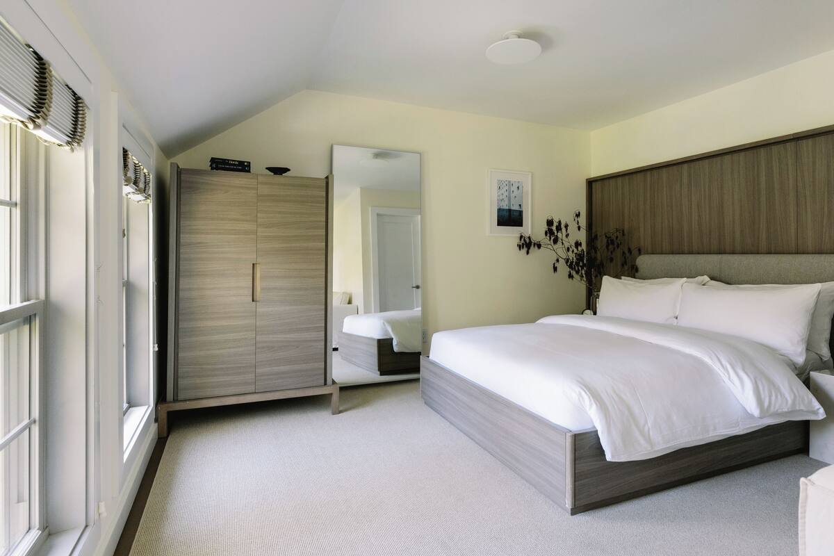 A bedroom with a bed, a wardrobe, a mirror, and a window.