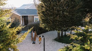 A house with a gravel driveway, a child holding an adult's hand, and a lamp post.