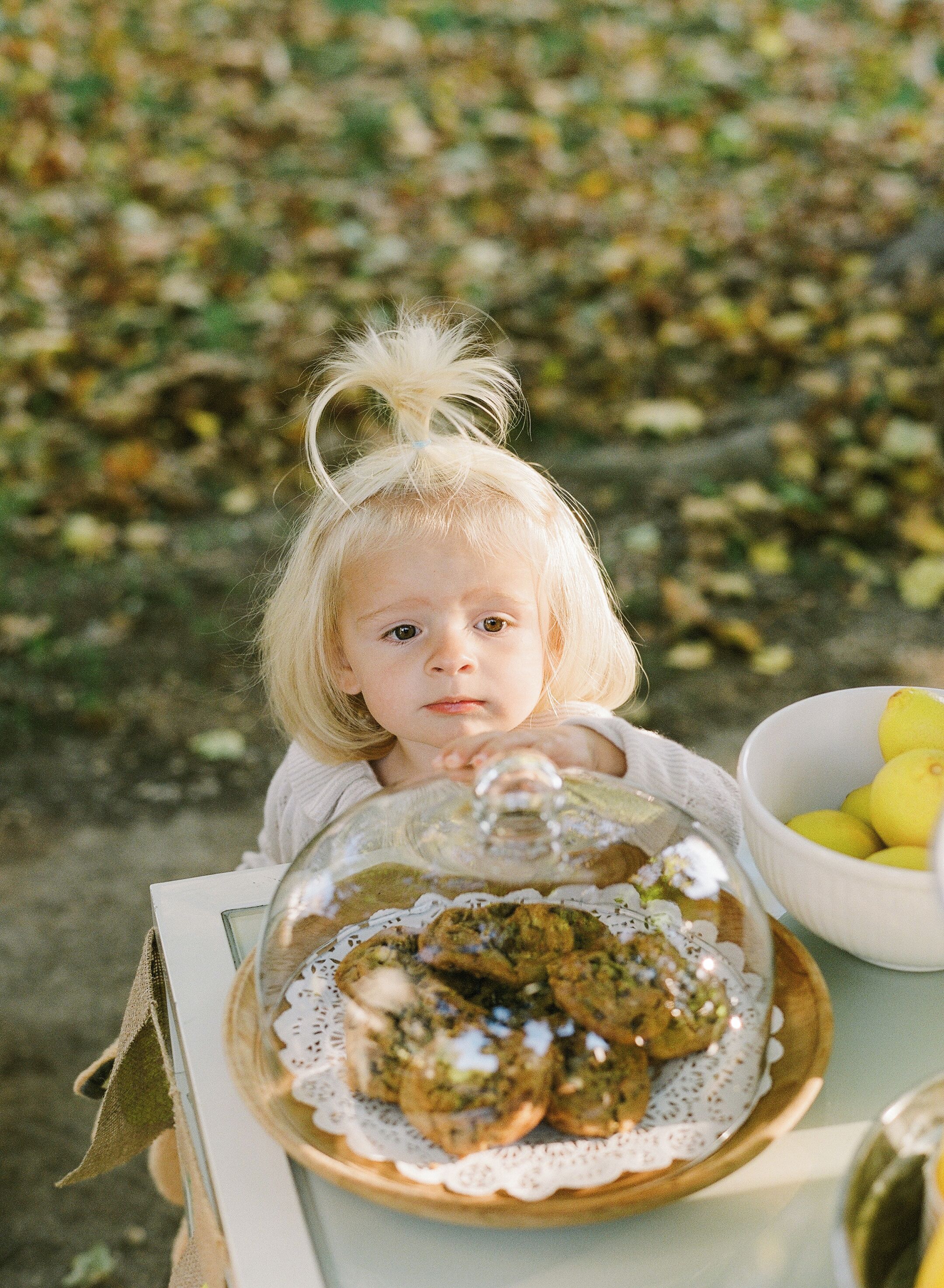 A child with a glass dome over a plate of food, outdoors with a blurred background of foliage.