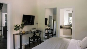 A modern bedroom with a bed, a desk with a chair, a television, and a large mirror.