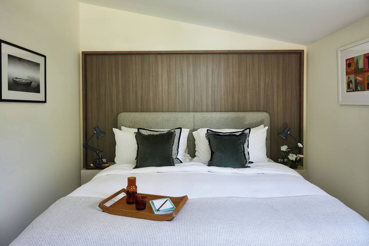 A neatly made bed with a tray of breakfast items, a bedside lamp, and a framed picture on the wall.